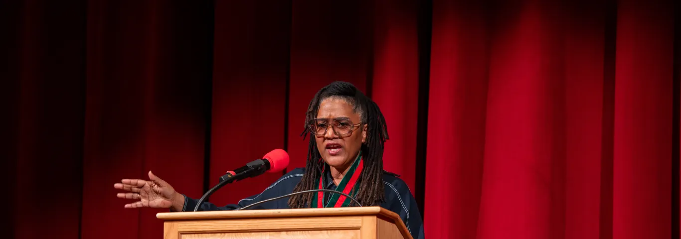 "a woman speaking at a podium in front of a red curtain"