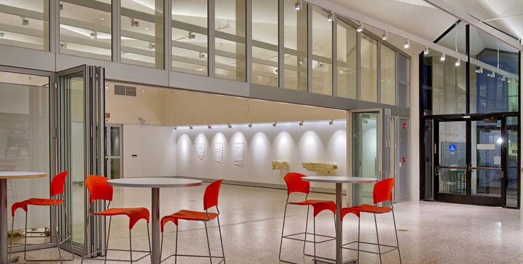 "interior gallery space with orange chairs and round tables"