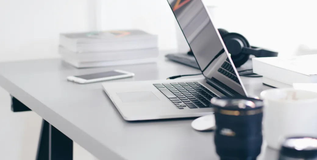 Photo of a workspace with computer, mug and stack of books