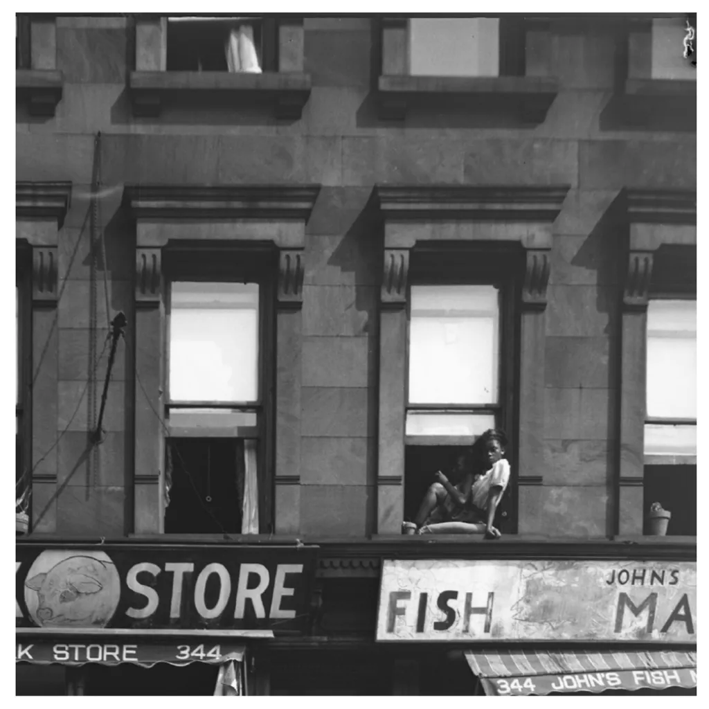 "Black and white photo of a child looking through a window onto the street below"