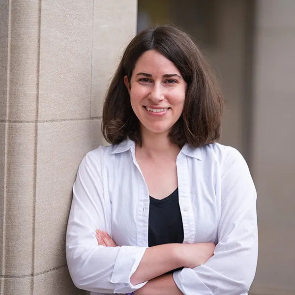 "woman wearing a white shirt over a black t-shirt in front of a stone column"