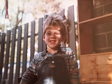 A photo of the author as a young boy, wearing Osh Kosh overalls and a big smile.