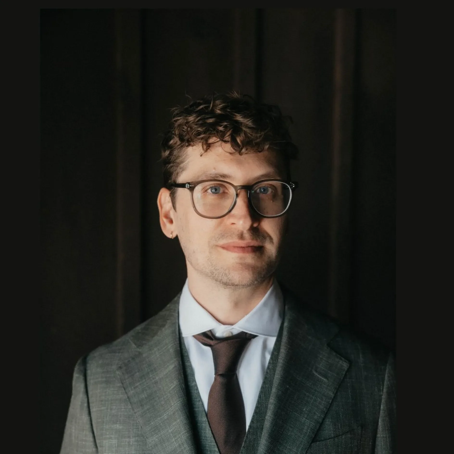 "man wearing a gray suit and tie against a dark background"