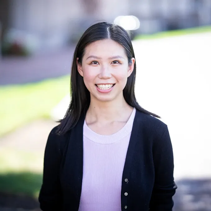"woman wearing a black sweater and lilac shirt in an outdoor setting"