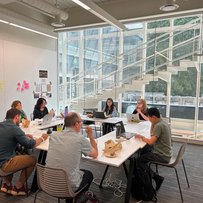 "A group of people sitting with laptops around a square table"