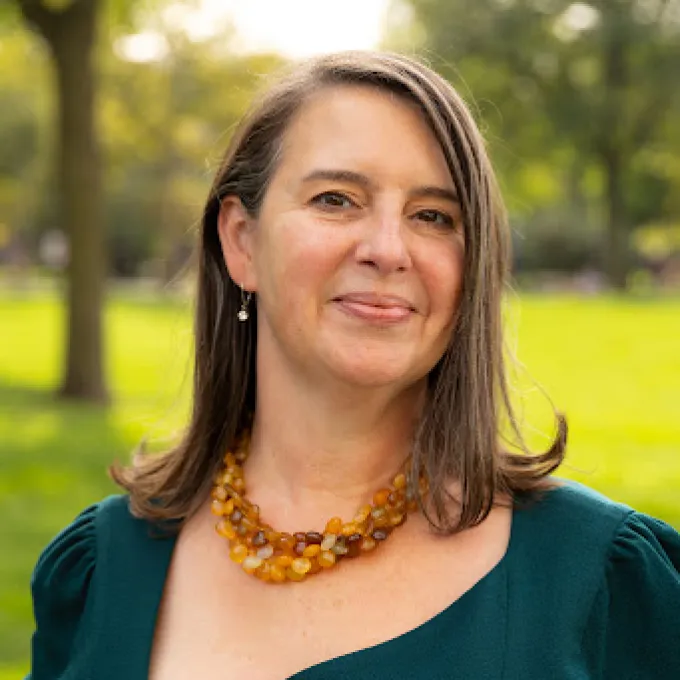 "Woman in a teal dress and amber necklace in an parklike setting"
