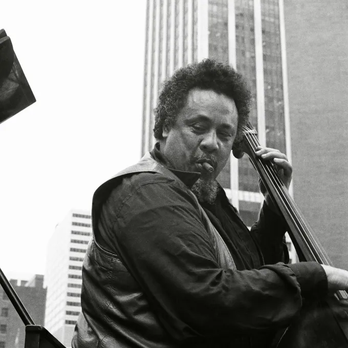 Black and white photo of Charles Mingus playing his standup bass in an outdoor urban setting